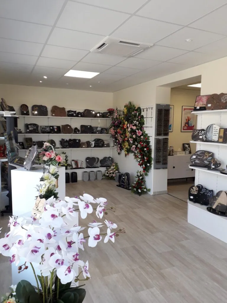Magasin d'articles funéraires avec orchidées blanches au premier plan et plaques commémoratives