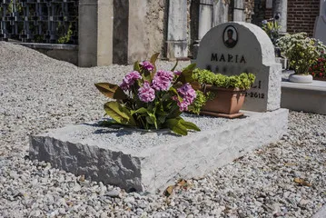Monument funéraire simple en pierre claire avec pot de fleurs et stèle arrondie
