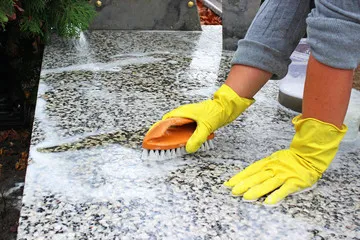 Nettoyage à la brosse d'une pierre tombale en granit moucheté avec des gants de protection
