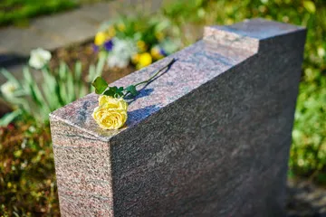 Rose jaune déposée délicatement sur le sommet d'une stèle funéraire en granit